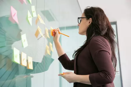 dogodki/confident-middle-aged-businesswoman-writing-sticker-with-pencil-brainstorming_1