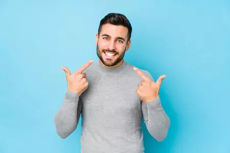 dogodki/young-caucasian-man-against-blue-wall-smiles-pointing-fingers-mouth_1